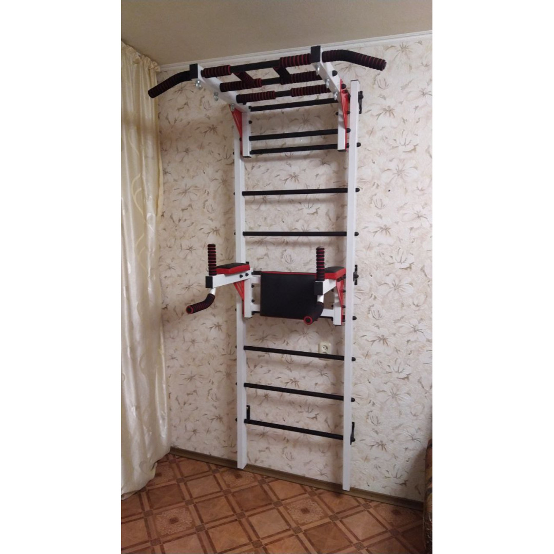 Drabinka gimnastyczna z poziomym drążkiem, drążkami i ławką ARTKOS jest w kolorze białym z czerwonymi i czarnymi elementami